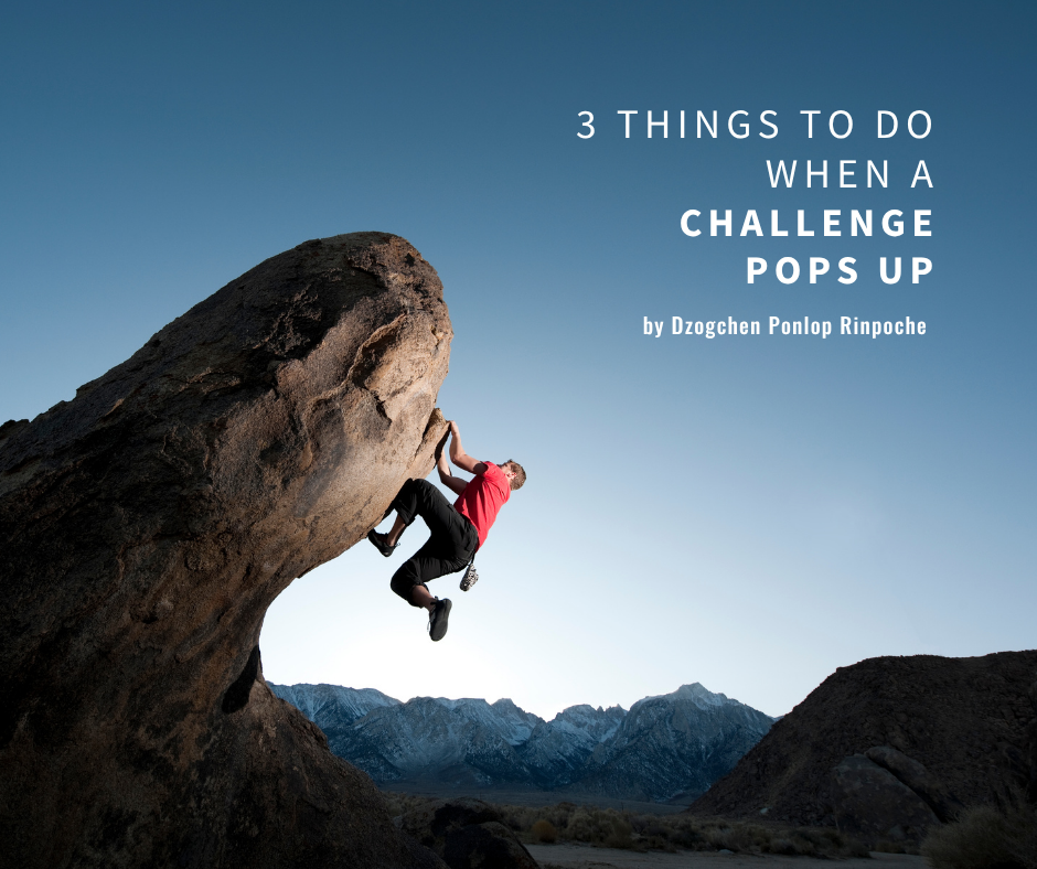 Rock climber wearing a bright red shirt and black pants clings with both hands and one shoe to a large rounded jutting rock in a mountain setting against a clear steel- blue sky.